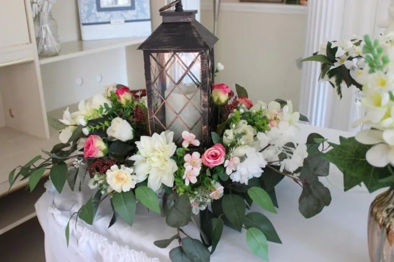 Wedding centrepiece of flowers and candle in a hurricane lamp holder on a table. 